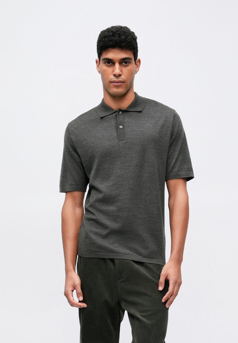 Dunkelgraues kurzärmeliges Poloshirt mit Kragen, ausgestattet mit zwei Knopfverschlüssen und einer glatten Textur. Kombiniert mit dunkelbraunen Cordhosen.