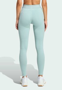 Högmidjade leggings i mjukt mintgrönt tyg med slät yta, figurnära passform och subtila sömnadsdetaljer, kombinerade med vita sneakers.