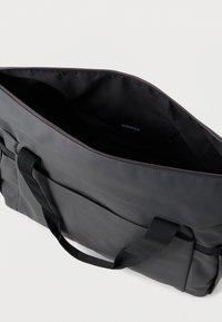 Sivi torba s crnim ručkama, prednjim džepom i otvorenom zip zatvaračem na glavnom dijelu koji prikazuje crnu unutrašnjost.