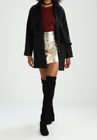 Chaqueta negra de gran tamaño, minifalda metálica plateada, top rojo con purpurina, medias de red y botas negras hasta la rodilla. Materiales texturizados y reflectantes.