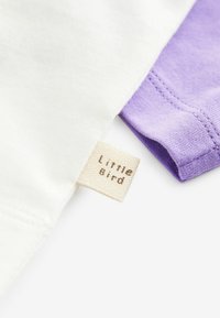 Bavlnená blúzka s bielym telom a fialovými rukávmi. Obsahuje textilný štítok s nápisom "Little Bird" v jednoduchom písmene.