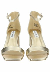 Sandali con tacco alto in metallo dorato, design open-toe, cinturino regolabile alla caviglia e tacco a blocco. Texture liscia e stile minimalista.