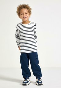 Gestreiftes langärmliges Hemd in Weiß und Marineblau, kombiniert mit Marineblauen Cargo-Hosen. Hat eine lockere Passform und bequeme Sneaker in verschiedenen Farben.