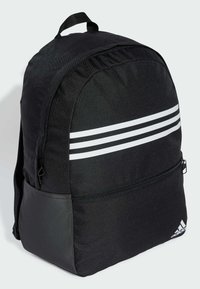 Zaino nero con design arrotondato, realizzato in tessuto resistente. Presenta tre strisce bianche e una tasca frontale con zip, logo del marchio nella parte inferiore.