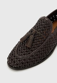 Brown woven leather shoe featuring a rounded toe, prominent tassels, and a sleek silhouette with contrasting stitching and sole.