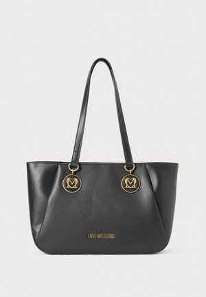Black faux leather tote bag with gold circular hardware, featuring double shoulder straps and embossed brand logo on the front.