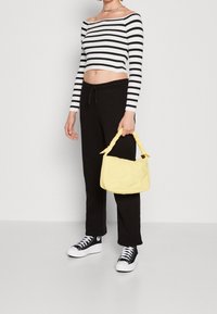 Top crop rayé noir et blanc à manches longues, associé à un pantalon noir et des baskets noires. Tient un sac à main jaune matelassé avec une anse torsadée.