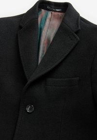 Blazer de lana negra con solapa con muesca, botón único y bolsillo en el pecho. El forro interior presenta un patrón geométrico en teal y rojo.