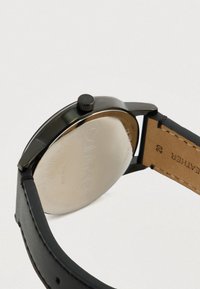 Schwarze Uhr mit einem glatten, runden Gehäuse und halbkugeliger Glasscheibe. Verfügt über ein Lederarmband und einen gravierten Gehäuseboden aus Edelstahl.