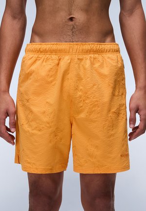 Orange swim shorts with textured fabric, elastic waistband, and a subtle leaf pattern. Includes a small logo on the lower side.