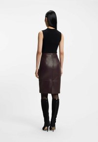 Top senza maniche nero abbinato a una gonna a matita in pelle borgogna con cerniera sul retro. Il modello indossa stivali neri con tacco al ginocchio.