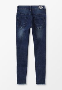Jeans ajustados de color azul oscuro con dobladillo deshilachado, dos bolsillos traseros con un diseño sutil y un parche de marca en la cinturilla.