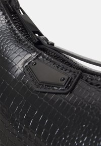 Sac à main en simili cuir noir avec une texture crocodile, doté d'une fermeture éclair et d'un détail en métal noir hexagonal.