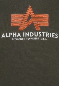 T-shirt nera con un logo arancione testurizzato contenente le lettere "A" e "F", e il testo "ALPHA INDUSTRIES, KNOXVILLE, TENNESSEE, U.S.A."