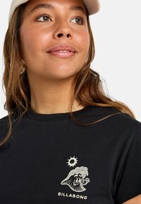 Zwarte katoenen T-shirt met een afbeelding van een cartoongolf en zon. Korte mouwen, ronde hals en subtiele gouden accenten in het ontwerp.