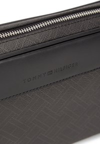 Μαύρο υφασμάτινο δερμάτινο πουγκί με ασημένιο φερμουάρ, ανάγλυφο λογότυπο της μάρκας και γεωμετρικό μοτίβο.