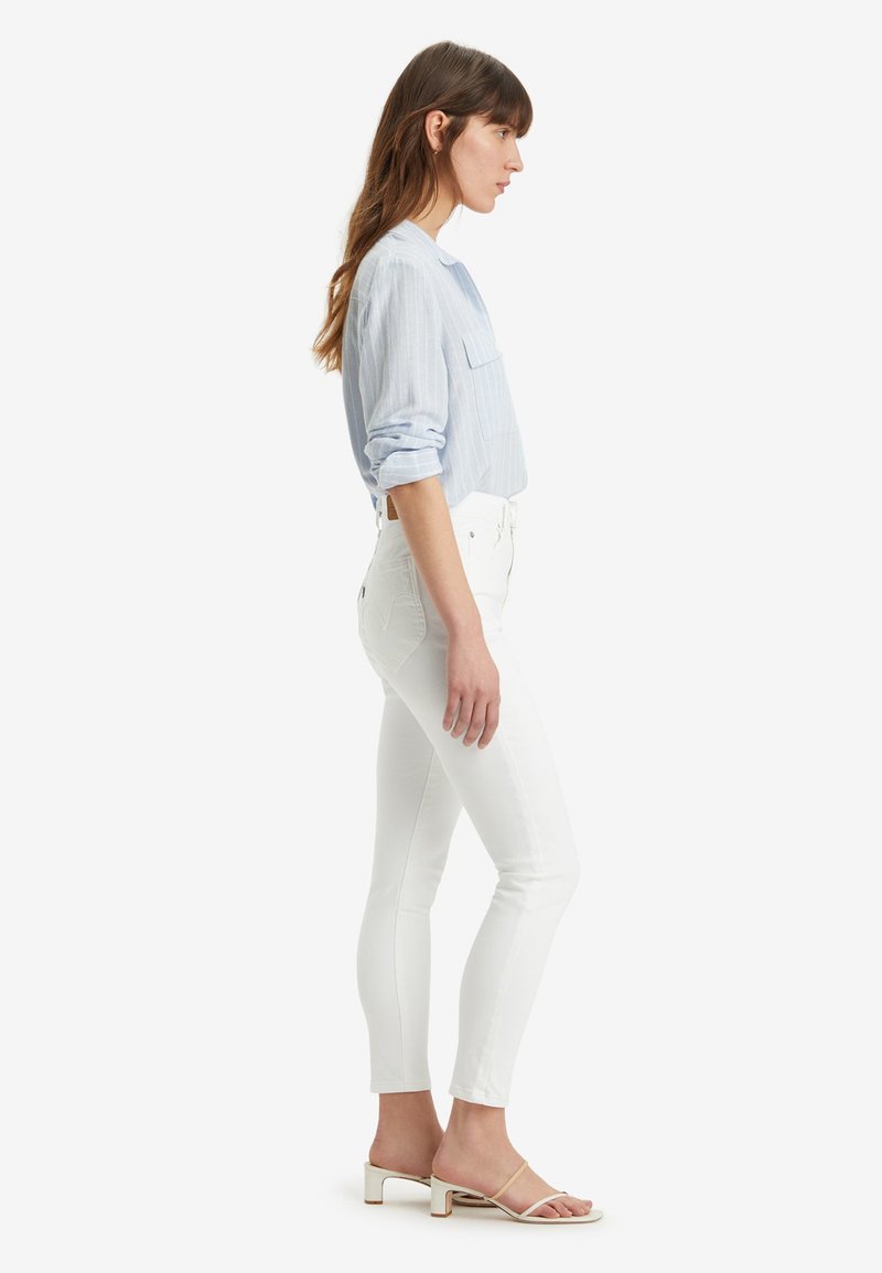 Camicia a righe blu chiaro a manica lunga con taschino sul petto, abbinata a jeans skinny bianchi a vita alta e sandali con tacco beige.