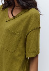 Olijfgroene V-hals T-shirt met korte mouwen, gemaakt van zachte stof met een zakdetail en opgerolde mouwen, met een gestructureerde afwerking.