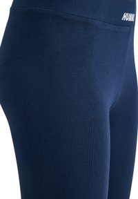 Leggings azul marino fabricados en tejido elástico, con una textura suave y una cintura alta que presenta el logo "HUMM". Sin patrones ni adornos visibles.