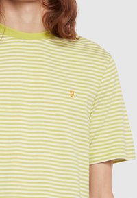 Camiseta de rayas verdes y blancas con mangas cortas, con un cuello redondo y un pequeño logo naranja en el pecho.
