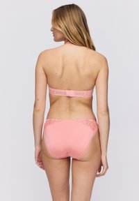 Vaaleanpunainen bikinit-sarja, jossa on niskalenkillinen yläosa ja siihen sopivat alaosat. Alaosissa on kukkakuvioista pitsiä vyötärön ympärillä.