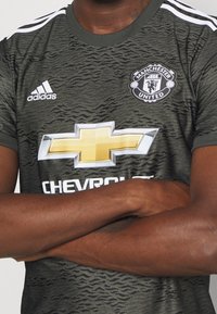 Vihreä kamouflage-urheilupaita valkoisilla raidoilla, jossa on suuri kultainen Chevrolet-logo ja Manchester Unitedin vaakuna rinnassa.