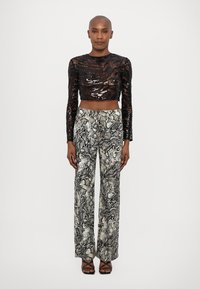 Fekete flitteres, hosszú ujjú cropped top, amely magas derekú, fekete, szürke és krémszínű kígyóbőr mintás nadrággal van párosítva.