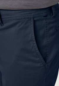 Dunkelblaue Hose aus strukturierter Stoff, mit Fronttaschen und dezenten Stickdetails für zusätzliche Langlebigkeit.