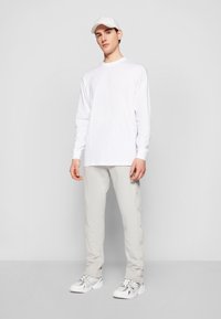 Long-sleeve white shirt, light gray pants with snap buttons, white sneakers, and a matching white cap. Simple, clean design with minimal details.