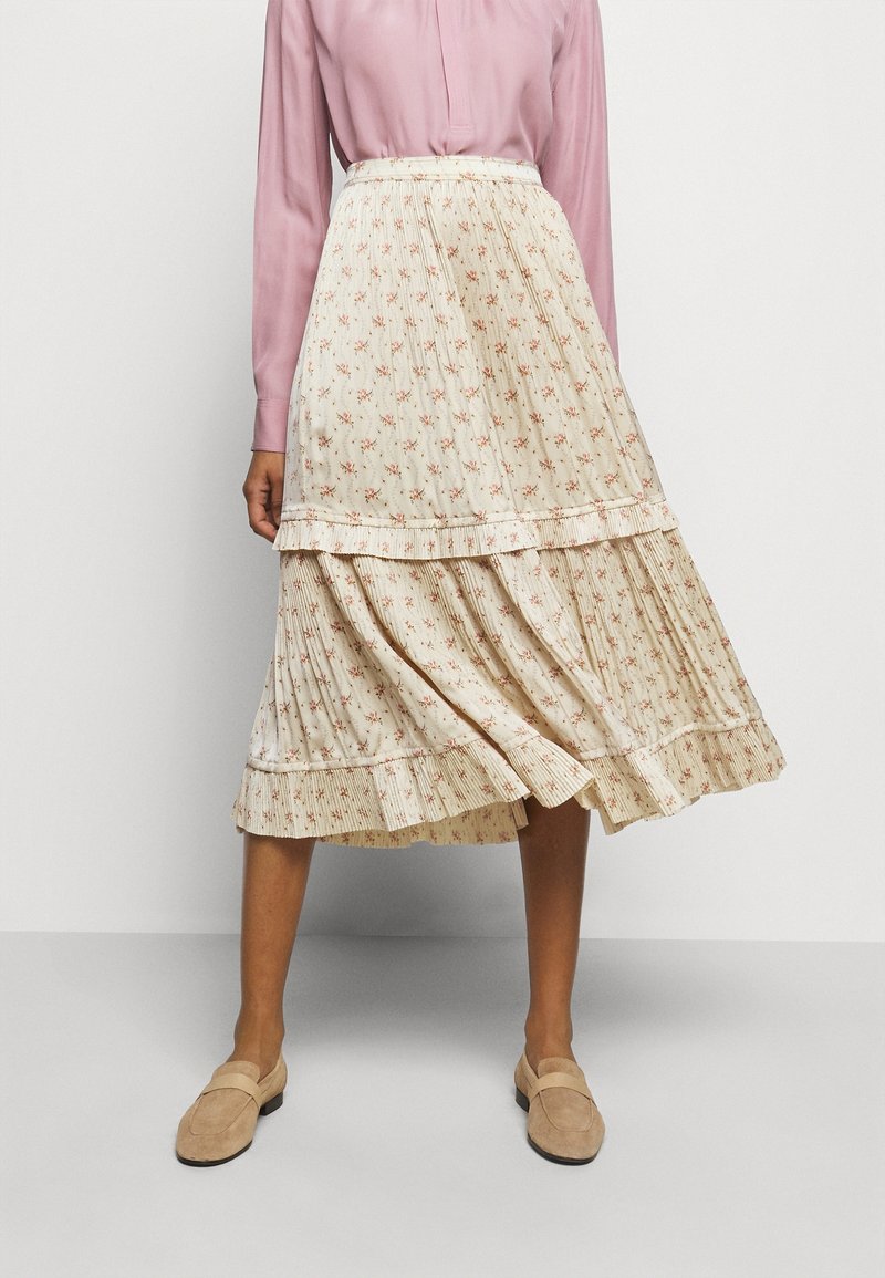 Falda midi floral en crema con patrones rojos y verdes, con un diseño de capas y pliegues texturizados. Combinada con una blusa rosa claro y mocasines beiges.
