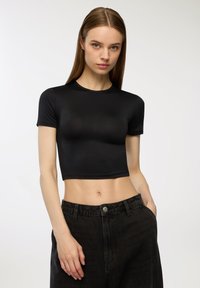 Czarny krótki top z krótkim rękawem o dopasowanym kroju, wykonany z gładkiego, elastycznego materiału, zestawiony z ciemnymi dżinsami z wysokim stanem.