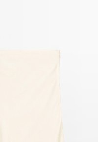 Tissu beige drapé verticalement, texture lisse avec un léger reflet, présentant une couture et un détail de fermeture éclair dans le coin supérieur gauche.