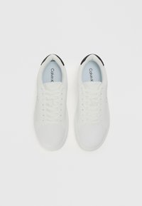 Białe sneakersy o gładkim, skórzanym wykończeniu, zaokrąglonym nosku i płaskich białych sznurowadłach. Czarne akcenty na pięcie i jasnoniebieska wkładka.