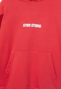 Rode sweatshirt met een voorzak en witte bedrukte tekst "STWD STUDIO" gecentreerd op de borst.