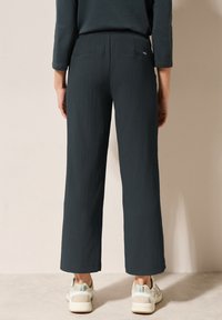 Pantalons larges texturés de couleur vert foncé avec une taille haute et deux poches arrière, associés à des baskets de couleur claire.