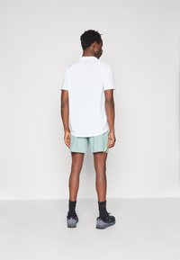 Λευκή αθλητική μπλούζα με κοντά μανίκια, μέντα σορτς και μαύρα αθλητικά παπούτσια. Περιλαμβάνει διακριτό λογότυπο στη μπλούζα και στις εξωτερικές ραφές των σορτς.