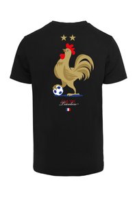 Sort t-shirt med et stort guld hane grafik, der sparker til en fodbold, med to guldstjerner ovenfor og "Équipe Tricolore" nedenfor.