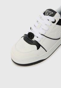 Bijela tenisica s crnim naglascima, teksturirani bijeli materijal, ravni đon, kružni crni logotip i bijele vezice.