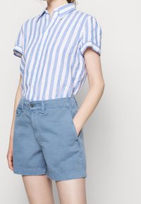 Kortärmad skjorta med knapper och blåvitrandigt mönster, kombinerad med ljusblå shorts som har framfickor och en avslappnad passform.