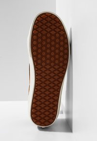 Brązowa gumowa podeszwa buta z diamentowym wzorem, biała śródpodeszwa i teksturowane akcenty po bokach, widziana z góry na jasnym tle.