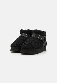 Sorte shearling ankelstøvler med rund tå, der har en sort læderrem prydet med metalnitter. Gummisål for godt greb.