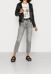 Zwarte leren motorjack over een witte graphic T-shirt met Mickey Mouse, gecombineerd met grijze high-waisted jeans en zwarte sandalen.