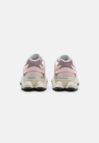 Pink suede sneakers with white mesh accents, a thick cream sole, and a prominent rounded rear design featuring a silver logo embellishment.