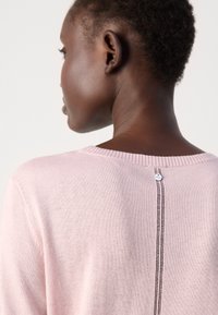 Light pink sweater with a smooth texture, round neckline, and a decorative line of stitching along the spine featuring a small tag.