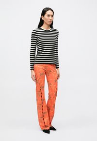 Pruhovaný čierno-biely dlhý rukáv doplnený o široké nohavice s oranžovým kvetinovým vzorom, postrannými rozparkami a čiernou špicatou obuvou.