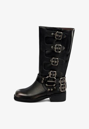 Botas de cuero negro hasta la rodilla con múltiples hebillas de plata, una correa con un anillo ovalado y un tacón bajo y apilado. Textura suave, diseño resistente.