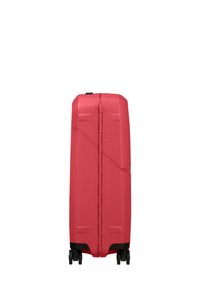 Hard-shell suitcase in bright red with a textured surface, designed with a vertical seam and four multi-directional wheels for easy maneuverability.