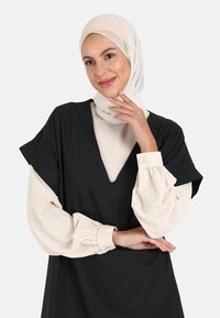 Black dress with a deep V-neck, short sleeves; layered with a beige long-sleeve top. Fabric has a smooth texture; features gathered sleeves.