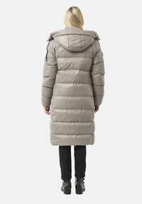 Lange, gewatteerde jas in lichtgrijs, met een capuchon, geribbelde manchetten en schuine naden. Draagt met zwarte broek en kniehoge laarzen.