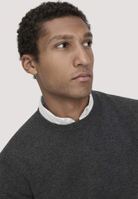Dunkelgrauer Pullover aus Strickstoff, Rundhalsausschnitt, über einem weißen Hemd mit Kragen getragen, strukturierte Optik, schlichtes Design ohne Muster.
